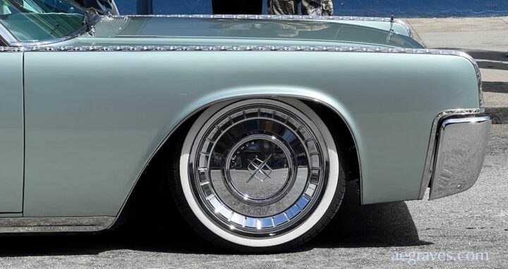 Pale sage green front right fender of a classic American car with etched chrome trim