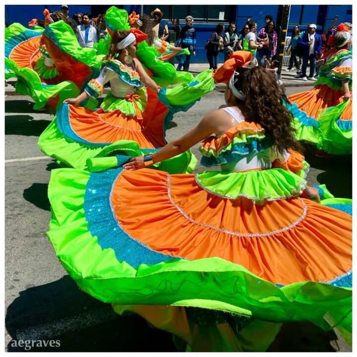 Dancers in orange, sequined teal, and lime green swirling with expansive skirts