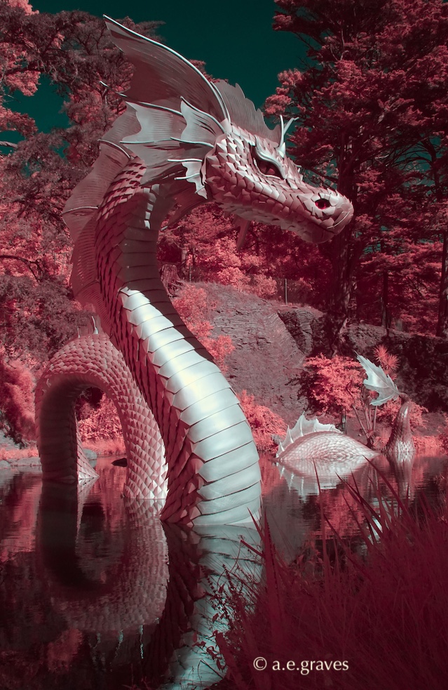 False color digital infrared image with vivid rose foliage behind a dragon sculpture emerging from a pond
