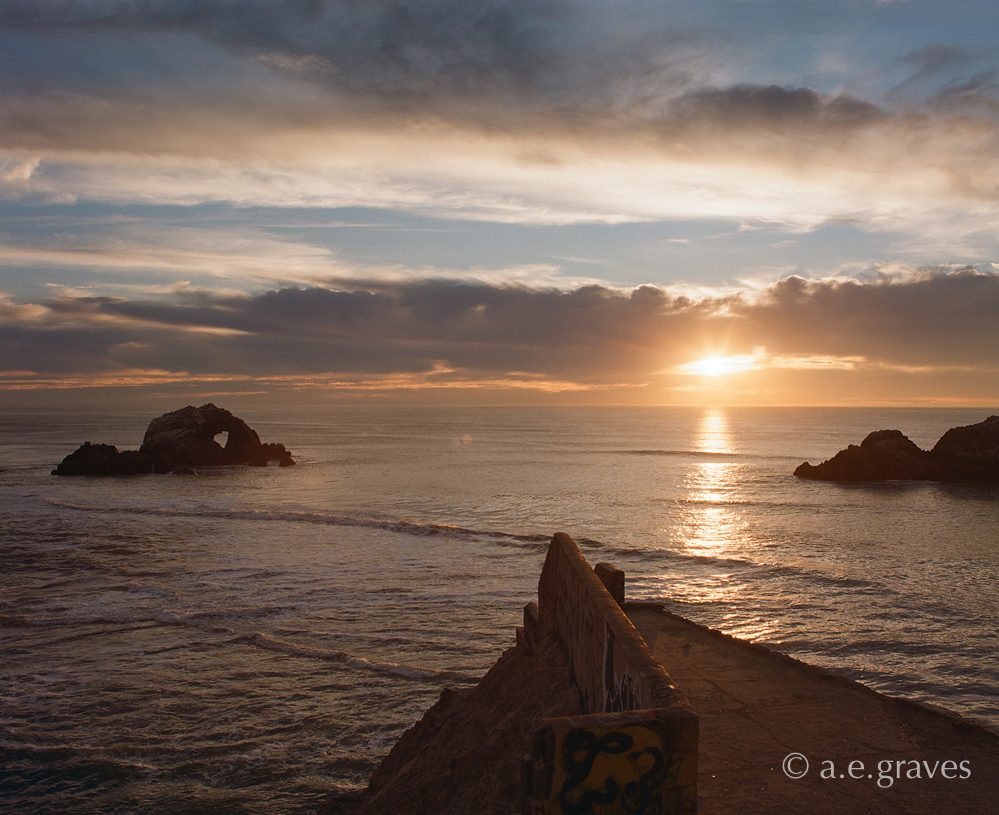 Sunlight breaks through the clouds and reflects on the Pacific above a ruined triangular patio pointing toward the horizon