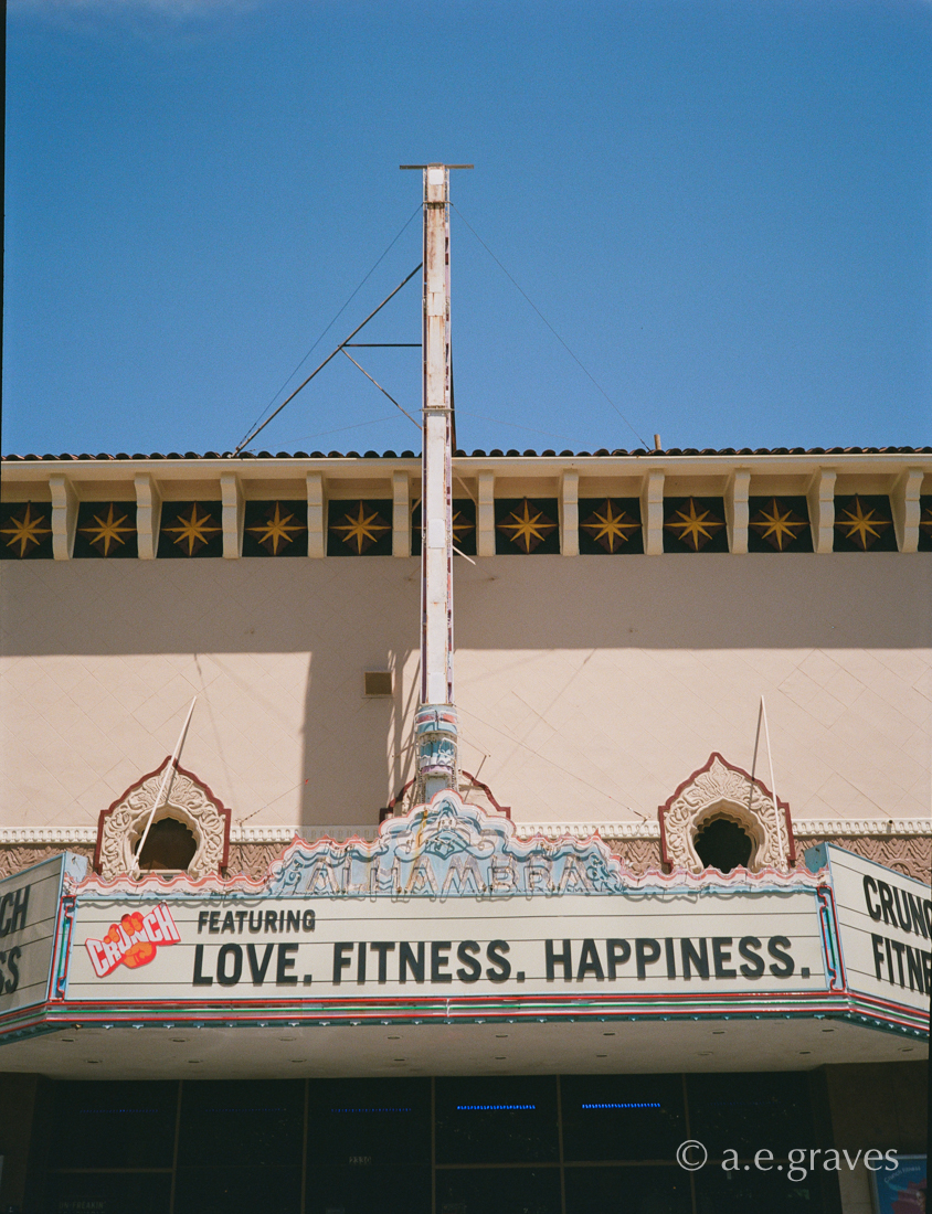 Elevation view of Alhambra theater marquee (shown as a vertical post) along with the signboard with elaborate neon and the faded pastel name, Alhambra