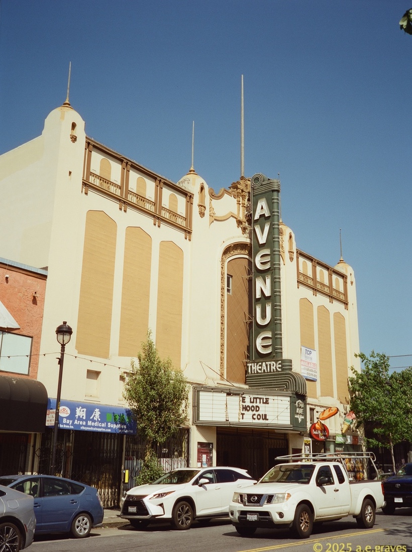 Street view of a cream and ochre movie theater with darker bronwn decorations, and a tall, green theater marquee with neon letters reading AVENUE