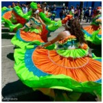 Dancers in orange, sequined teal, and lime green swirling with expansive skirts