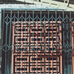 Red geometric wooden door behind a black metal security grate