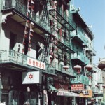 Vertical image of four storey buildings with green or multicolored metal balconies, flags, hanging lanterns with runners on the sidewalk running in the opposite direction