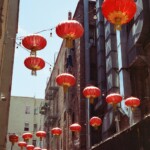 Color image of backlit red lanterns backed by tall brick buildings and ducts