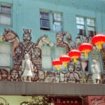 Glowing red lanterns hang in front of soldier sculptures and a related mural with a pale green background in SF Chinatown