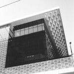 Nuanced dark areas are easily achieved, and detail is preserved well. This is a brighter image, and retaining detail in the brightest areas is also possible. A monochrome image of a building with metal screens with different types of perforations, plus a dark, reflective glass grid.