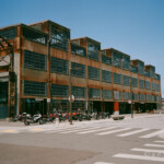 Vast eastern elevation of a four story industrial building with rusted metal panels and large windows made of small panels