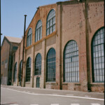 Color image of a wide brick building with 7 large, arched composite windows downstairs and three upstairs; the sun creates shadows beneath ledges and overhangs