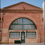 Sunlit one story brick building with a wide arched window and a tiny door