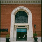Color image of the tall front entrance of the Contemporary Jewish Museum, a glass door surrounded by cream colored stone in a red brick wall