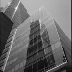 Monochrome image of a trapezoidal glass wall reflecting a geometric building