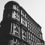 The brightly lid side of a dark gray building. Details render nicely. Monochrome image of a bright sky with a dark building covered in columns and framed windows