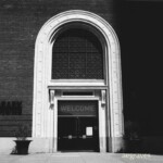 Entrance to SF's Jewish Contemporary Museum Monochrome image of a square glass door in a rectilinear frame surrounded by a bright, all white arch.