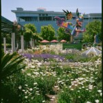 Color image of a blooming garden with a large, colorful, winged monster sculpture