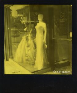 Monochrome black and yellow Polaroid image of mannequins wearing gowns in a reflective store window